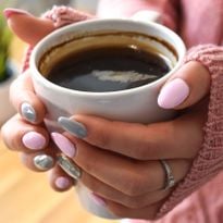 a pair of hands with pink-polished nails holding a cup of black coffee