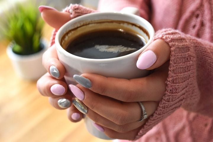 a pair of hands with pink-polished nails holding a cup of black coffee