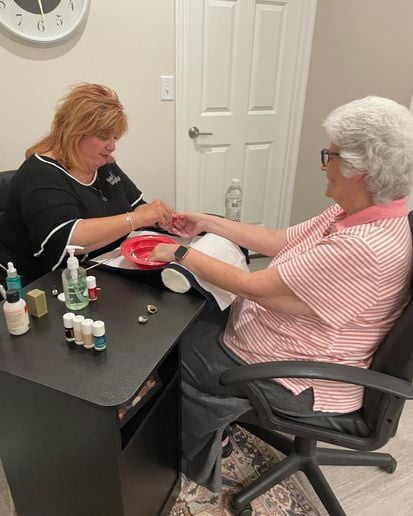 Two women face each other over a manicure table, as one woman gives the other woman a manicure.